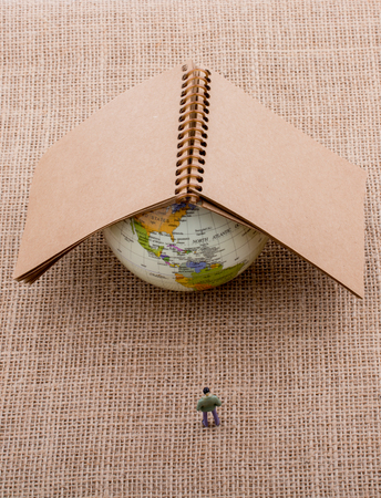 Figurine and globe with a notebook on the top of itの写真素材