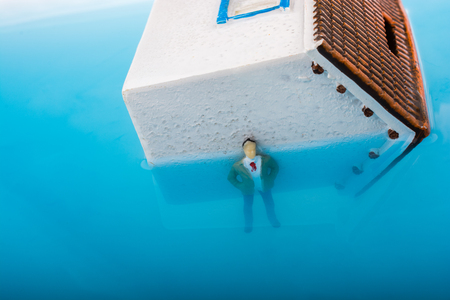 Man figurines in water by the side of a little model houseの写真素材