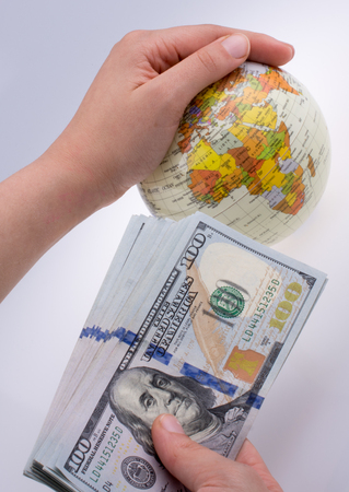 Human hand holding American dollar banknotes by the side of a model globe on white backgroundの写真素材