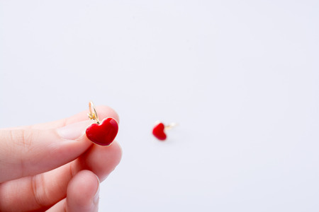 Red color heart shape earring in hand on whiteの写真素材