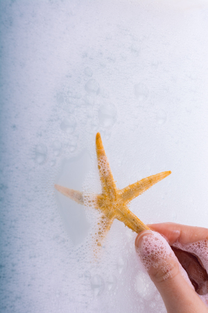 Hand holding starfish in water covered with foamの写真素材