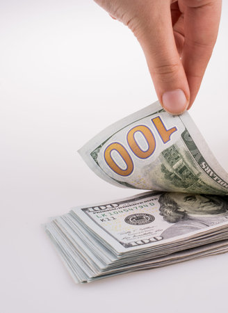 Human hand holding American dollar banknotes by the side of a model house on white background