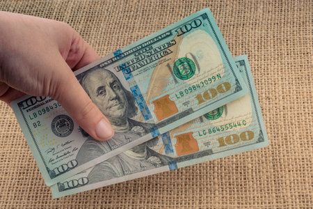 Hand holding banknote bundle of US dollar on a linen canvas background