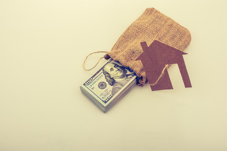 Paper house placed beside a bundle of US dollar banknoteの写真素材
