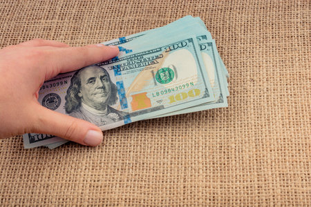Hand holding banknote bundle of US dollar on a linen canvas background