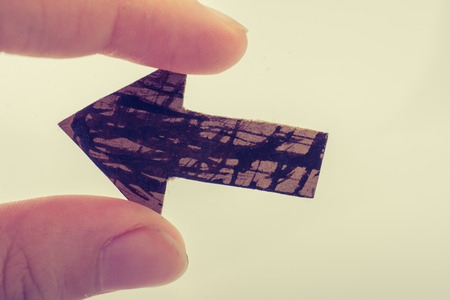 Arrow cut out of brown paper in hand on whiteの写真素材