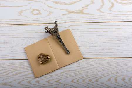 Eiffel tower miniature and a steel heart on a brown notebook on a wooden backgroundの写真素材