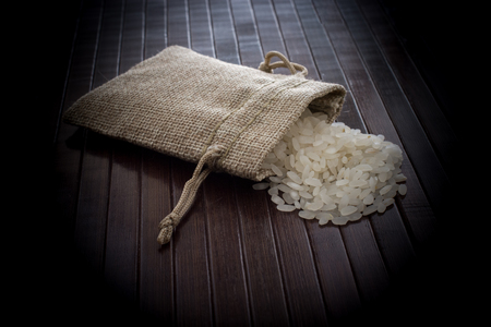 A straw pouch full of uncooked rice on a wooden backgroundの写真素材