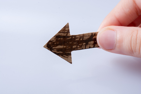 Arrow cut out of brown paper in hand on whiteの写真素材