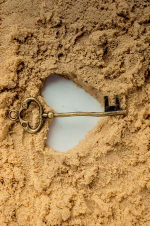 Retro style key and a heart shape made on brown sandの写真素材