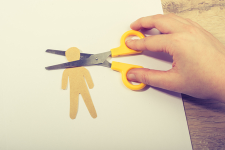 Scissors cutting paper man's head on white paper on wooden backgroundの写真素材