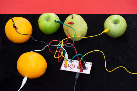 Cables connected to a device and to apples, oranges and pears on displayの写真素材