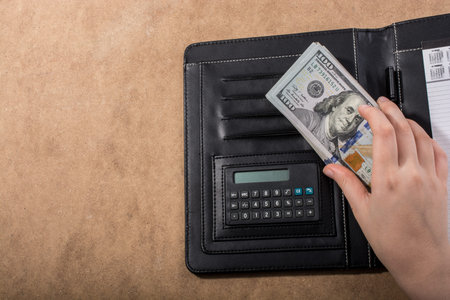 Hand holding American dollar banknotes beside a calculator