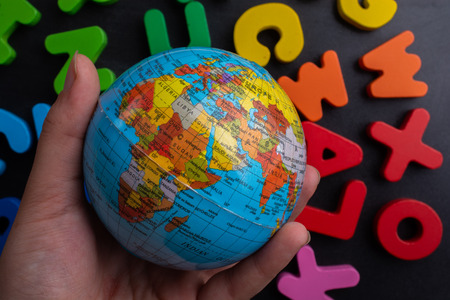 Hand holding an earth globe model on colorful letters on a black backgroundの写真素材