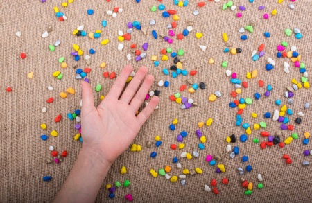 Hand placed on colorful pebbles on canvas background