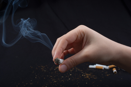 Hand is holding smoking cigarette with smoke aroundの写真素材