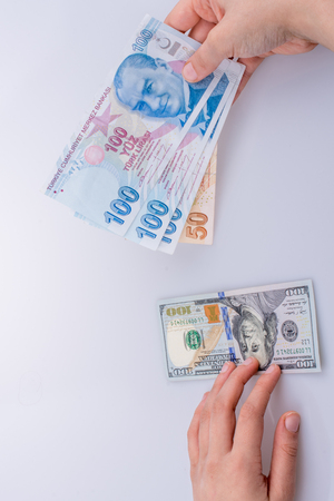 Hands holding American dollar banknotes and Turksh Lira banknotes side by side on white backgroundの写真素材