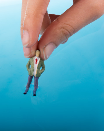 Hand holding a man   figurines in water by the side of  a Little model houseの写真素材