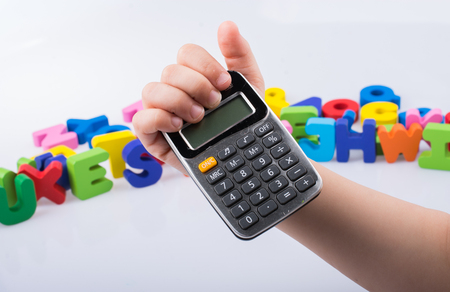 Little calculator in hand with colorful letters behind on whiteの写真素材