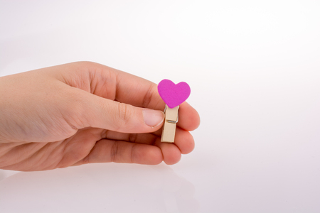 Hand holding a red clothespin with a heartshape on a white backgroundの写真素材