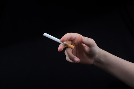 Hand is holding a cigarette on black backgroundの写真素材