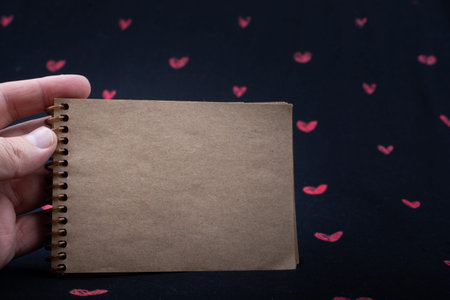 Spiral brown notebook on background with red hearts