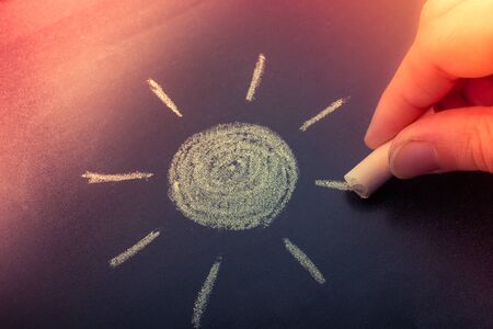 Hand drawing sun by chalk with light ray shape on blackboard backgroundの写真素材