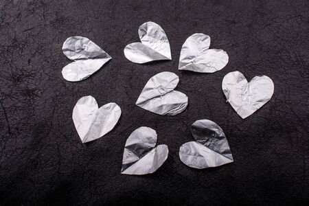 Heart shaped cut out mettalic paper pieces on black backgroundの写真素材