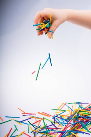 Hand letting coloured wooden  sticks fall on white backgroundの写真素材