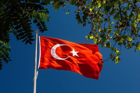 Turkish national flag with white star and moon on a pole in skyの写真素材