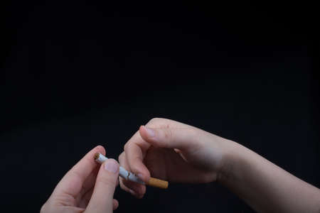 Hand is breaking a cigarette on a black backgroundの写真素材