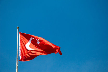 Turkish national flag with white star and moon on a pole in skyの写真素材