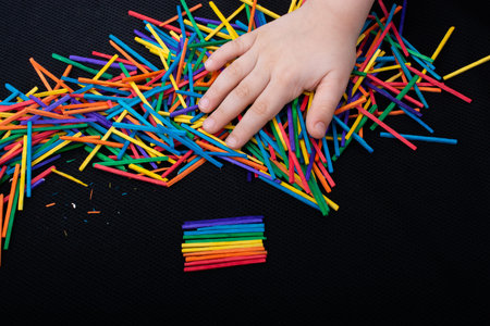 Kid playing with coloured wooden  sticks for creativity on white background