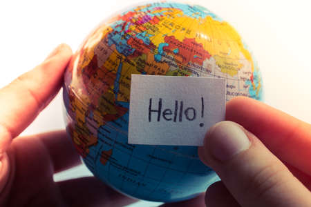 Hand holding notepaper with HELLO wording on model globeの写真素材