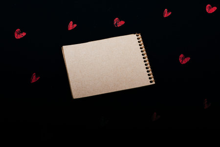 Spiral brown notebook on background with red hearts