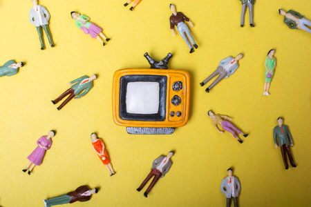 Figurine people around retro syled tiny television on yellow backgroundの写真素材