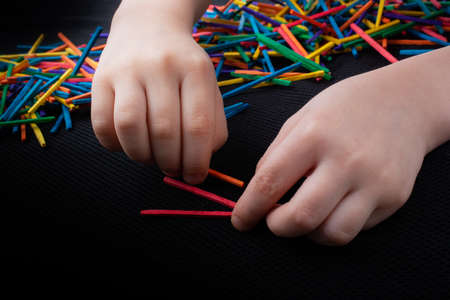 Kid playing with coloured wooden  sticks for creativity on white backgroundの写真素材