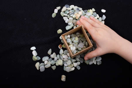 Hand filling the box with stone pebbles gravels on a black backgroundの写真素材