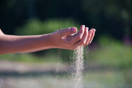 Female hands releasing dropping sand. Sand flowing through the hands against blue ocean. Summer beach holiday vacation conceptの写真素材