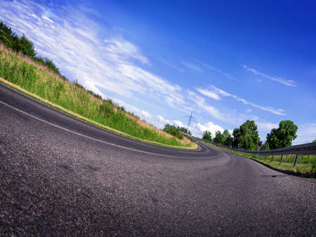 a curved road with blue sky in landscapeの写真素材