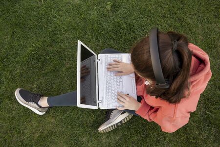 Girl sitting in park on the green grass with laptopの写真素材