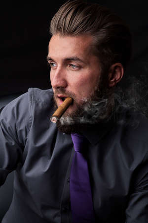 Portrait of a young businessman successful smoking a cigar on black backgroundの写真素材