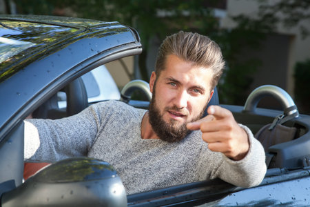 Young man in a car is pointing at you