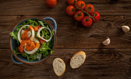 A bowl of fresh salad and tomatoes on a wooden tableの写真素材