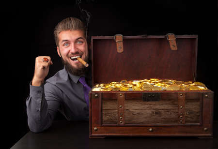 Attractive business man with a gold chest full of goldの写真素材