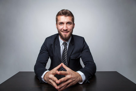Attractive business man is sitting on his desktop and smiles