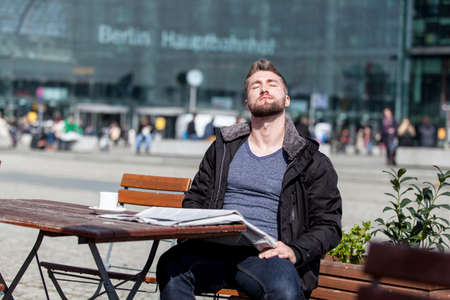 Attractive young man is sitting in a coffee shop taking a sunbathの写真素材
