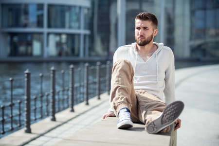 Attractive man with beard is sitting on a wall in Berlinの写真素材