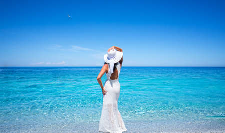 Young woman in a white dress is standing on a tropical beachの写真素材