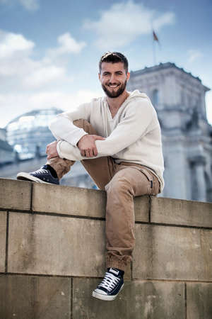 Attractive man is sitting on a wall in front of a famos buildingの写真素材